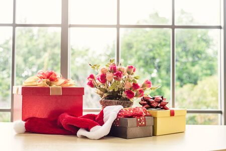 Christmas gifts with rose vaseand santa hat on wooden table interior of room view through window with tree Background with Copy Space,Decoration During Christmas and New Year.の写真素材