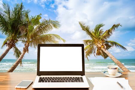 Mockup of laptop computer with empty screen with smartphone and coffee cup on wooden on table at landscape early sunrise over blue the sea background,working on the beach,Freelance work and holidayの写真素材