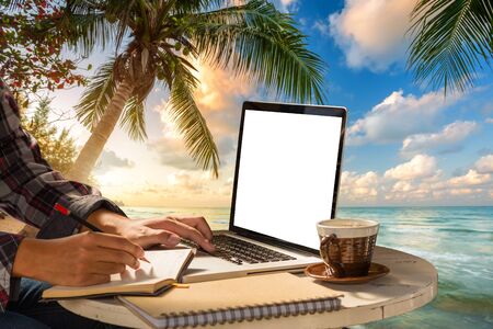 businessman hand write make a note of notebook working with laptop computer, coffee on table at landscape early sunrise over blue the sea background,working on the beach,Freelance work and holiday.の写真素材