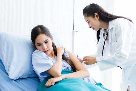 Asian young female doctor with syringe to the arm of Asian young female patient on Bed for better healing In the room hospital background.の写真素材