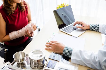 Close-up of Young man doctor therapeutic advising with laptop of checking splint the arm of female patient hand due to with her arm broken for better healing sit in a wheelchair In the room hospital.の写真素材