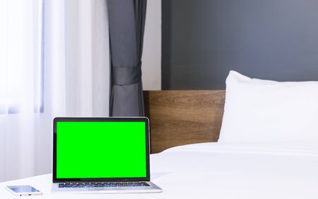 Laptop computer with blank green screen with smart phone on white bed decoration in hotel bedroom interior background,Work and business in leisure with travel in the holiday concept.の写真素材