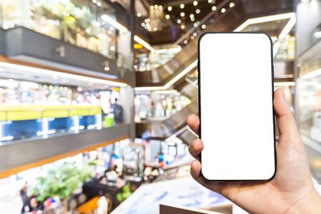 Close-up of female use Hand holding smartphone with empty blank white screen blurred images touch of Abstract blur of inside shopping complex background,shopping online concept.の写真素材