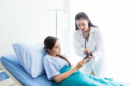 Asian young female doctor therapeutic advising with tablet to Asian young female patient on Bed in hospital background.の写真素材