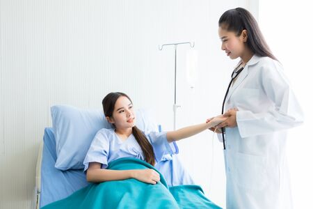 Asian young female patient on bed while doctor hands of checking examining his pulse for record the treatment results in hospital background.の写真素材