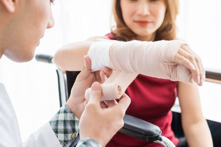 Close-up of man doctor with wrapping nurse bandages splint to the arm of a female patient wear arm splint with analogue pressure gauge for better healing In the room hospital background.の写真素材