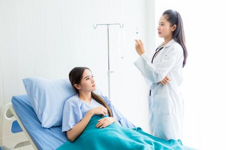 Asian young female doctor with syringe to Asian young female patient on Bed for better healing In the room hospital background.の写真素材