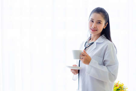 Portrait of asian young female doctor eating coffee from a cup and stethoscope with in hospital background.の写真素材