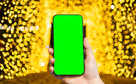 Close-up of female use smartphone blurred images with Yellow Colorful light Abstract circular bokeh of Christmas tree background Decoration During Christmas and New Yearの写真素材