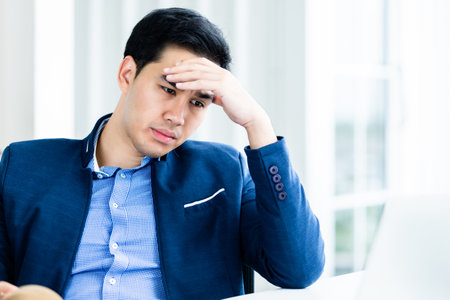 Stressed businessman worked with laptop computer and having a headache after business losses In the office room background.の写真素材