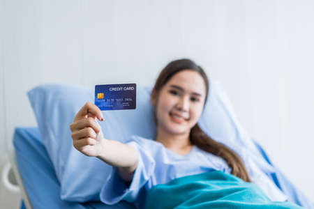Asian young female patient smiley face Abstract blur with focus on show holding a credit card lying on bed in the room hospital background,payment medical treatment conceptの写真素材