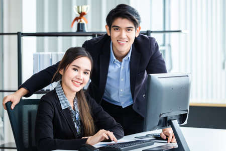 Happy couple of businesswoman and businessman partners discussing positive adult business working together with computer on wooden table and ideas at meeting in office background.の写真素材