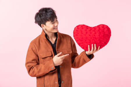 Valentine's day concept, Asian a man handsome young holding a red heart shaped pillow in love isolated on pink blank copy space studio background.の写真素材