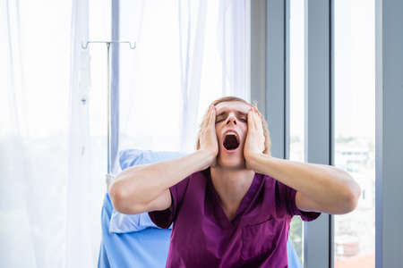 a man patient have headache and Have a fever with anxiety face lying on bed in the room hospital background.の写真素材