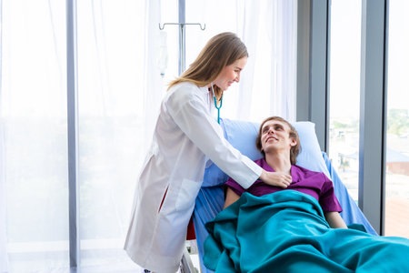 female doctor with hands of checking examining his pulse to a man patient on bed for record the treatment results with smiley face very good symptom in hospital background.の写真素材