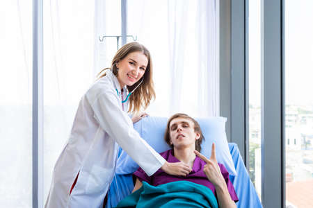 a man patient on bed show showing thumbs up with smiley face very good symptom to female doctor in hospital background.の写真素材
