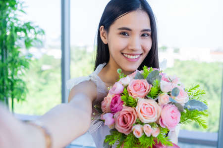 Valentine's day concept, Selfie of Happy of smiling Asian young female sitting at a table food holding a bouquet of roses at in the restaurant backgroundの写真素材
