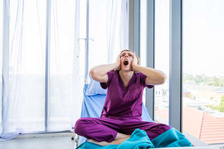 a man patient have headache and Have a fever with anxiety face lying on bed in the room hospital background.の写真素材
