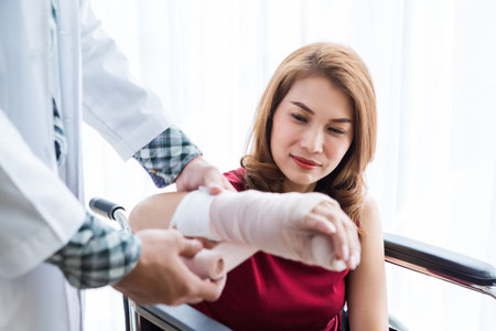 Close-up of Young man doctor of checking splint the arm of female patient hand due to with her arm broken for better healing sit in a wheelchair In the room hospital background.の写真素材