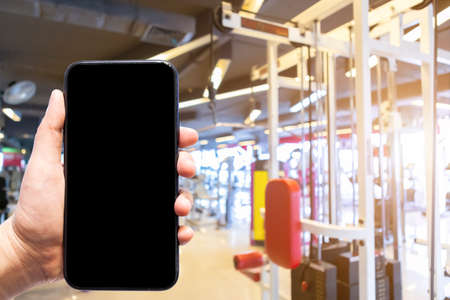 Close-up of female use Hand holding smartphone blurred images touch of Abstract blur of defocused sport gym interior and fitness health club with sports exercise equipment Gym blur background.の写真素材