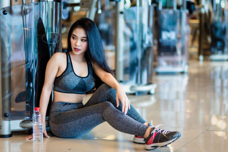 Fitness Asian women sitting in sport gym interior and fitness health club with a bottle of water.の写真素材