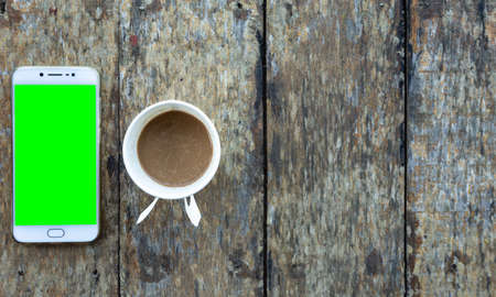 Green screen Smartphone and Coffee cup made of paper on old wood desk on top view.の写真素材