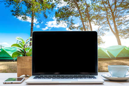 Mockup of laptop computer with empty screen with coffee cup and smartphone on table in forest summer camp among meadow on Mountain,recreation and Tourist holiday outdoor conceptの写真素材