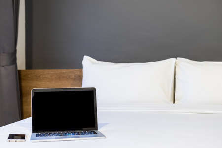 Laptop computer with blank screen with smart phone on white bed decoration in hotel bedroom interior background,Work and business in leisure with travel in the holiday concept.の写真素材