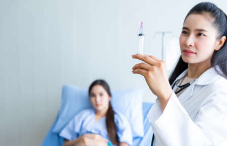 Asian young female doctor with syringe to Asian young female patient on Bed for better healing In the room hospital background.の写真素材