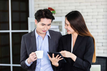 Happy successful of Young Asian businesswoman and businessman partners while working together with a tablet and business man holding a cup of coffee in office background,Working coupleの写真素材