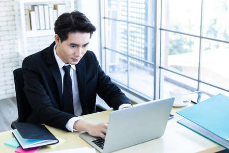 Happy of asian young businessman see a successful business plan on the laptop computer and pen on wooden table background in office,business expressed confidence emboldenの写真素材