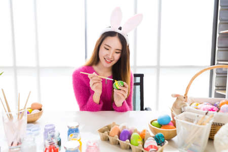 Easter holiday concept, Happy Asian Young woman wearing bunny ears hand painted eggs for Easter with colorful Easter eggs In the white room backgroundの写真素材