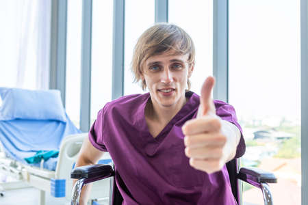 a man patient sit in a wheelchair Abstract blur with focus show showing thumbs up with smiley face very good symptom in hospital background.の写真素材