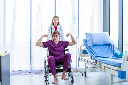 a man patient sit in a wheelchair show showing thumbs up with smiley face very good symptom and female doctor therapeutic advising with positive emotions in hospital background.の写真素材