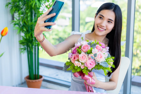 Valentine's day concept,Selfie of Happy of smiling Asian young female sitting at a table food holding a bouquet of roses at in the restaurant backgroundの写真素材