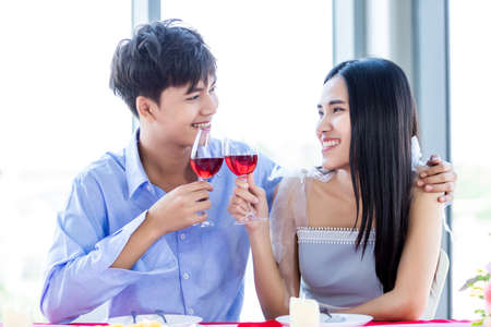 Valentine's day concept,Happy Asian Young sweet couple having romantic the Lunch with clinking toasting wine glasses at the restaurant background.の写真素材