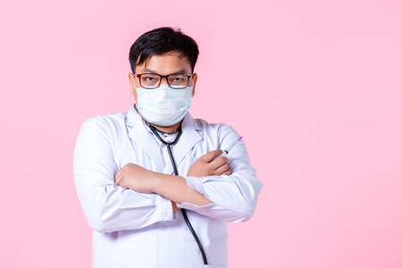 Asian man doctor therapeutic,stethoscope advising with positive emotions advising with arms folded and holding a syringe to the side eyes looking at camera in isolated on pink blank copy spaceの写真素材