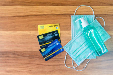 Blue Protective disposable medical mask,Credit cards and alcohol hand sanitizer on wooden background,Top view office table,Concept of Prevention of the spread of COVID-19 virus infectionの写真素材