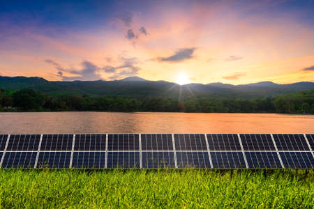 Photovoltaic modules solar power plant with lake views green forested mountain with evening blue dramatic sunset sky background, Alternative energy concept.の写真素材