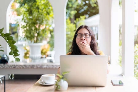 asian of freelance business female bored yawning in front of casual working with laptop computer and coffee and smartphone in coffee shop like the background,covering her mouth out of courtesyの写真素材