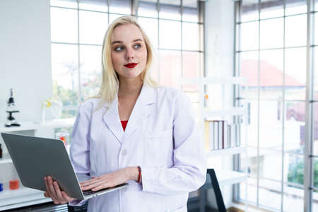 portrait of a female researcher carrying working with laptop computer and out research in a chemistry lab scientist holding test tube with sample in Laboratory analysis backgroundの写真素材
