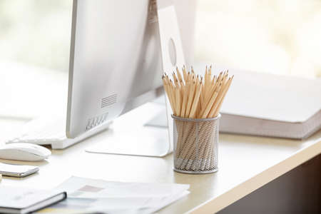 Brown color pencils in basket,notebook on wooden white table and computer monitor and office equipment background,workplace concept.の写真素材