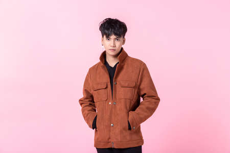 fashion Portrait of Confident handsome young Asian man with keeping hands in pockets of pocket the side eyes looking at camera in isolated on pink blank copy space studio background.の写真素材