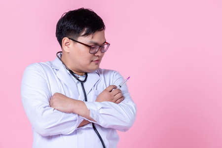 Asian man doctor therapeutic,stethoscope advising with positive emotions advising with arms folded and holding a syringe to the side eyes looking at camera in isolated on pink blank copy spaceの写真素材