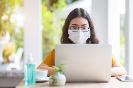 freelance people business female wearing protective mask casual working with laptop computer in coffee shop like the background,working from home,Concept of Prevention of the spread of COVID-19 virusの写真素材