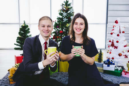 Happy new year 2021 concept, Happy couple holding the having cup of coffee,milk or chocolate in Christmas and New Year's Eve party Christmas tree background After finishing business workの写真素材