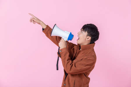 Asian a man handsome young wearing shouting with megaphone to the side eyes looking at camera in love isolated on pink blank copy space studio background.の写真素材
