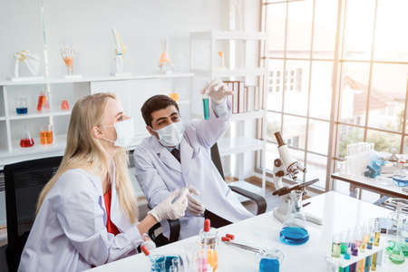 Two scientists are working holding looking at test tube with sample in a chemistry lab scientist or young female and male researcher are doing investigations in Laboratory analysis backgroundの写真素材