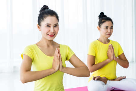 Two young Asian women workout practicing yoga in yellow dress or pose with a trainer and practice meditation wellness lifestyle and health fitness concept in a gym.の写真素材
