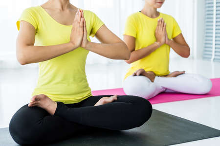 Close-up of Two young Asian women workout practicing yoga in yellow dress or pose with a trainer and practice meditation wellness lifestyle and health fitness concept in a gym.の写真素材